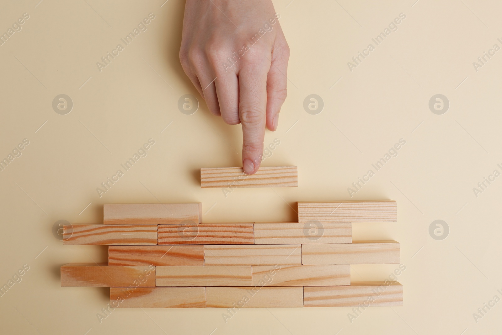 Photo of Woman finishing construction of wooden blocks on beige background, top view