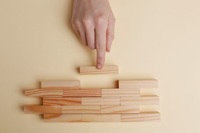 Woman finishing construction of wooden blocks on beige background, top view