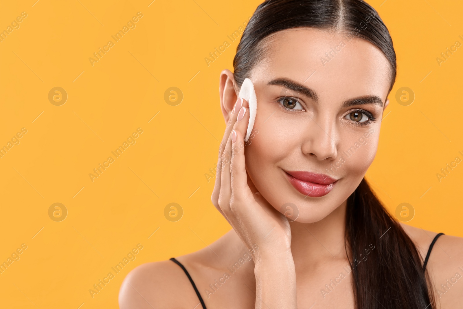 Photo of Beautiful woman removing makeup with cotton pad on orange background. Space for text