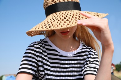 Young woman with straw hat against blue sky on sunny day