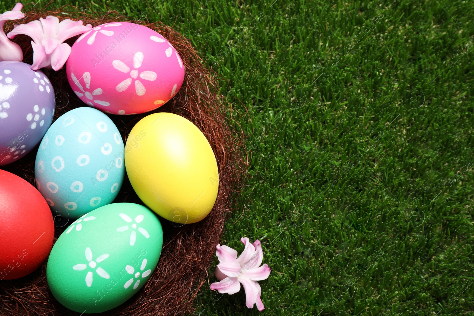 Photo of Colorful Easter eggs in decorative nest on green grass, top view. Space for text