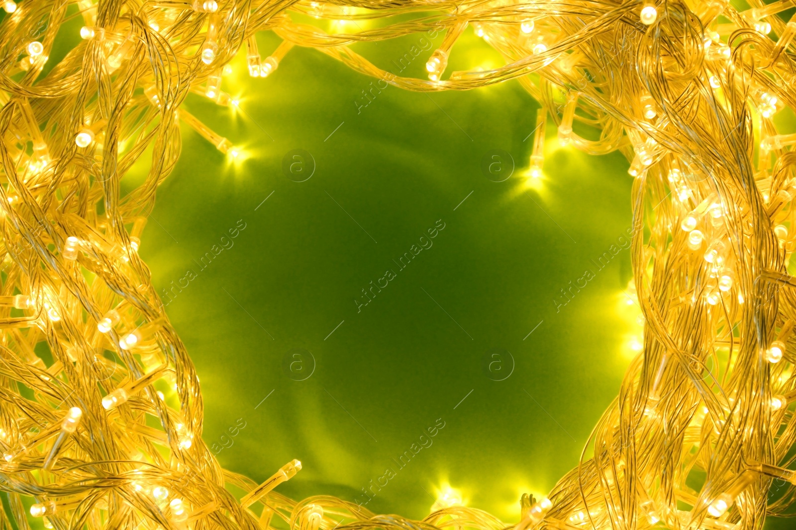 Photo of Frame made of glowing Christmas lights on green background, top view