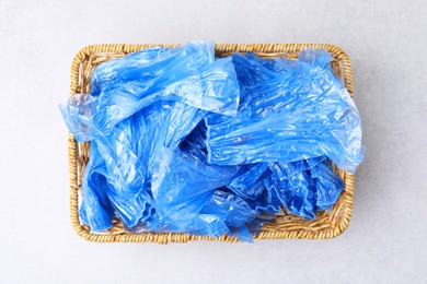 Photo of Blue medical shoe covers in wicker basket on light background, top view