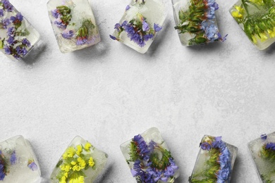 Photo of Ice cubes with flowers on light stone background, flat lay. Space for text