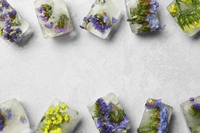 Ice cubes with flowers on light stone background, flat lay. Space for text