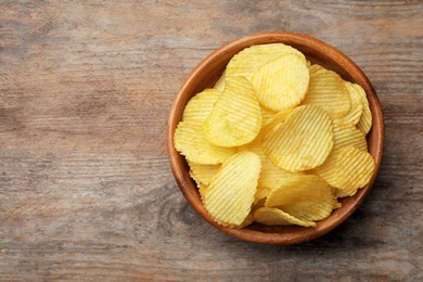Photo of Delicious crispy potato chips in bowl on table, top view with space for text