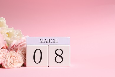 Photo of International Women's day - 8th of March. Wooden block calendar and beautiful flowers on pink background, space for text