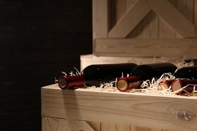 Photo of Wooden crate with bottles of wine on dark background, closeup