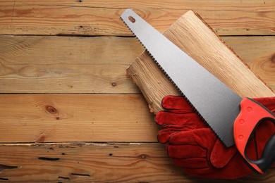 Photo of Saw with colorful handle and gloves on wooden background, top view. Space for text