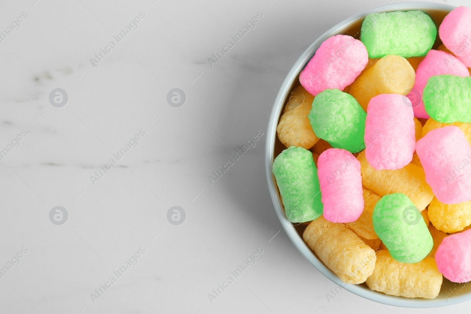 Image of Bowl with colorful corn puffs on white marble table, top view. Space for text