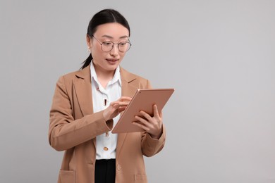 Portrait of beautiful businesswoman with tablet on grey background. Space for text