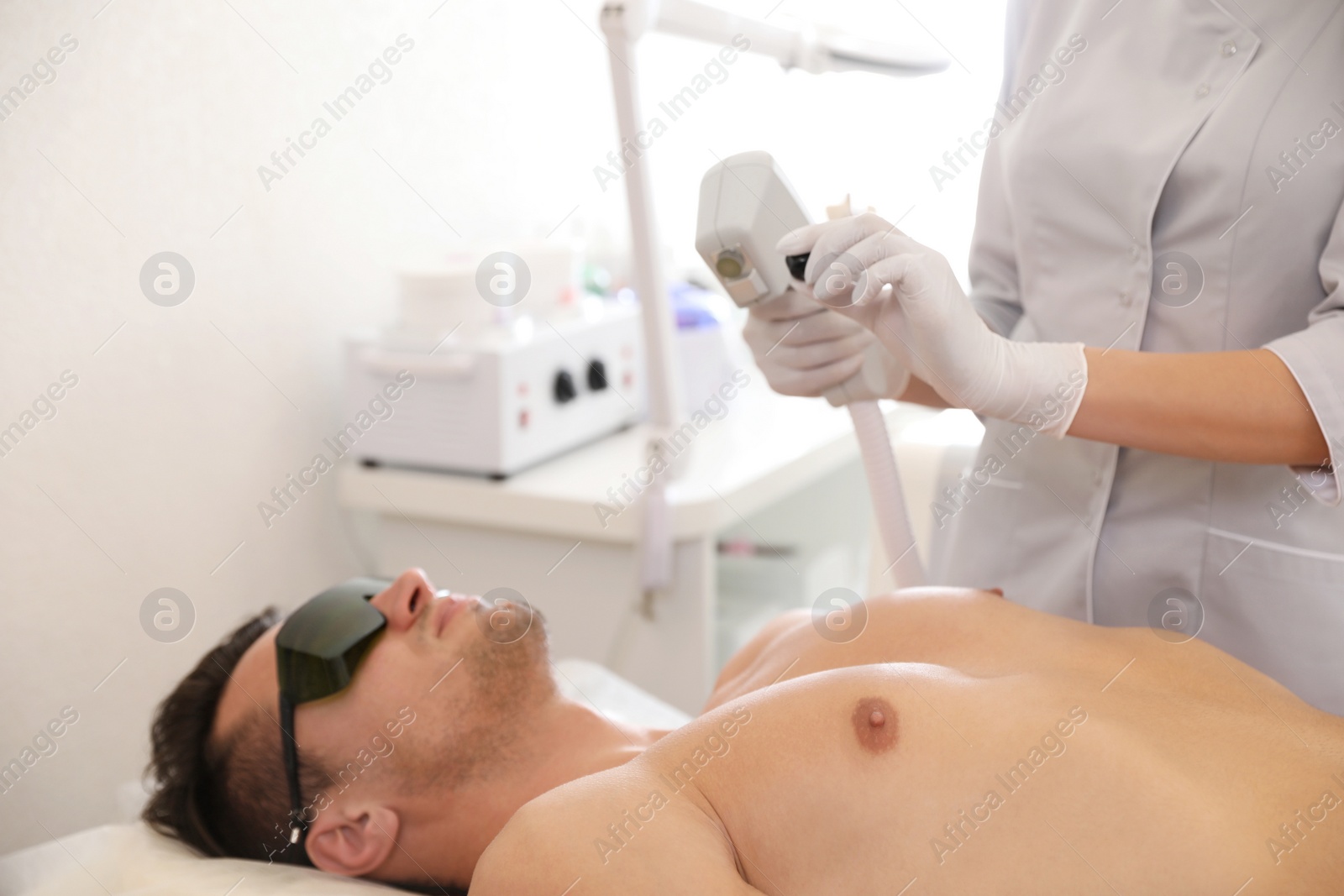 Photo of Young man undergoing laser epilation procedure in beauty salon