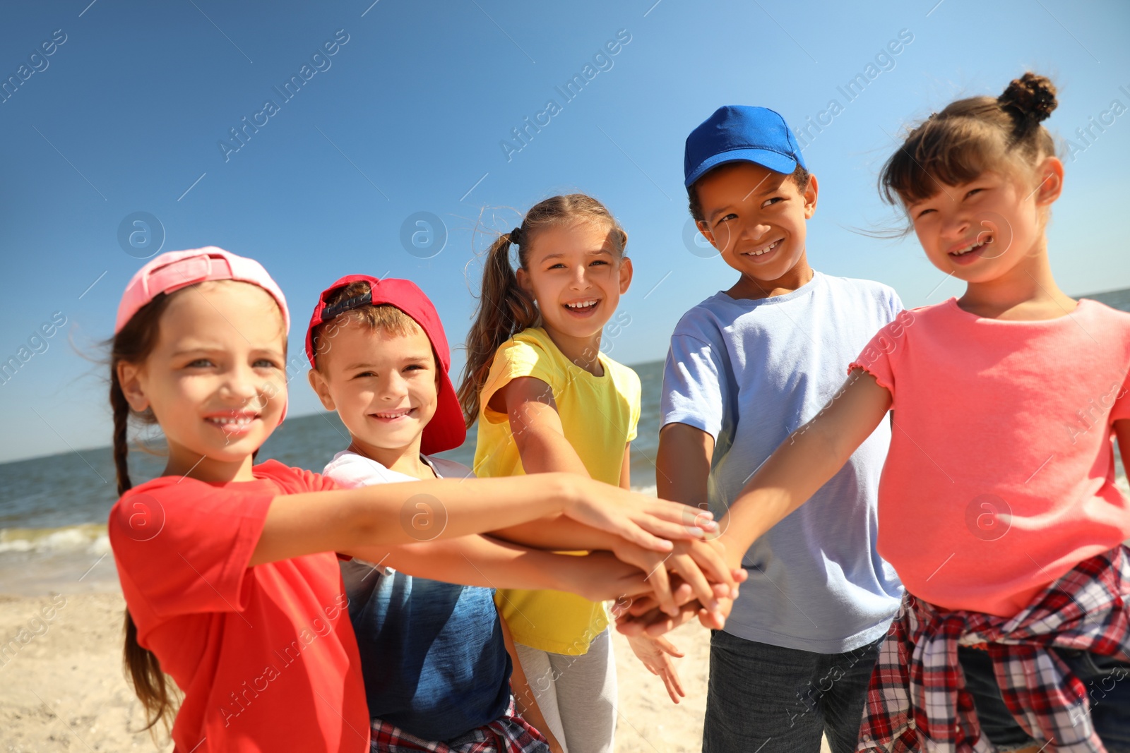 Photo of Group of children putting hands together at sea beach on sunny day. Summer camp