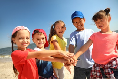 Group of children putting hands together at sea beach on sunny day. Summer camp