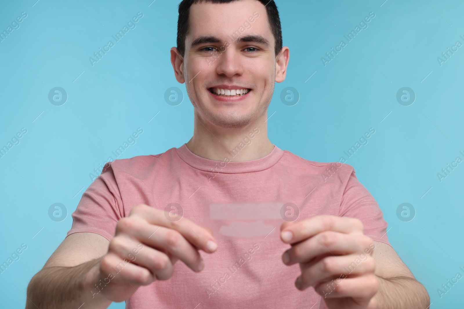 Photo of Young man with whitening strips on light blue background