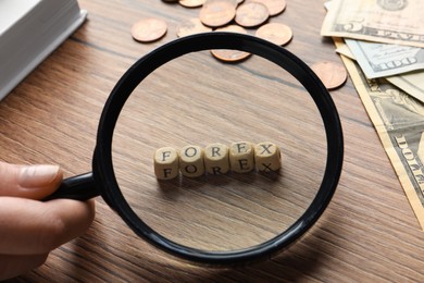 Photo of Woman looking through magnifying glass at word Forex made of cubes with letters on wooden table, closeup