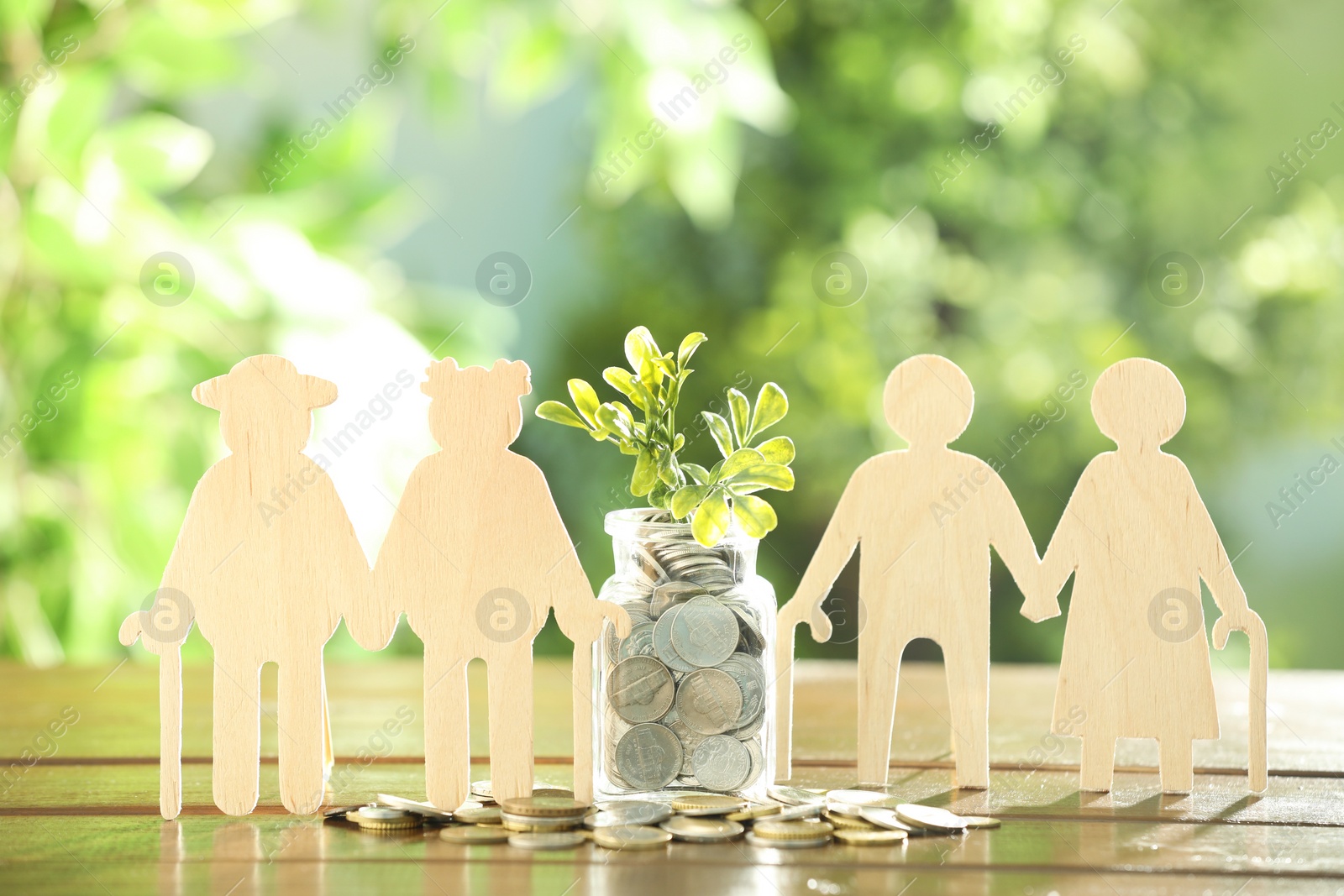 Photo of Pension savings. Figures of senior couples, coins and green twigs on wooden table outdoors