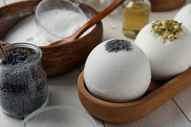 Photo of Different bath bombs and ingredients on white wooden table, closeup