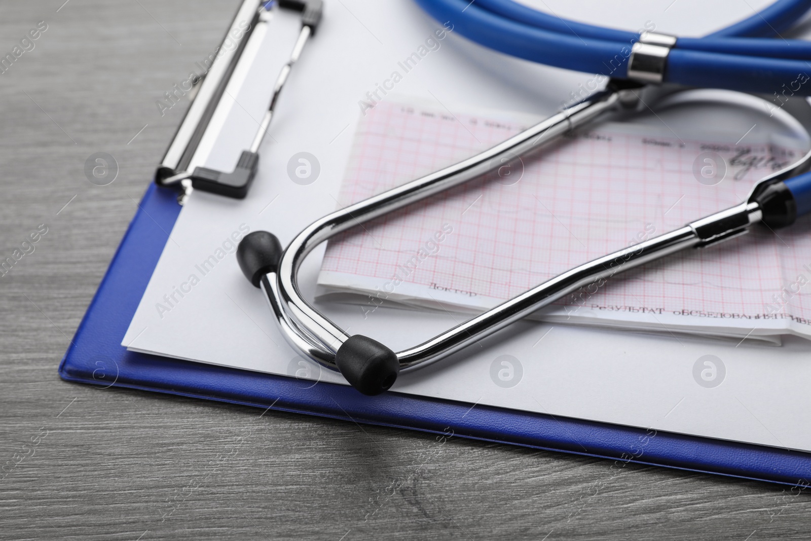 Photo of Clipboard with stethoscope and cardiogram on wooden table, closeup