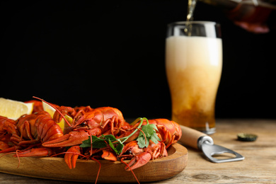 Photo of Delicious red boiled crayfishes and beer pouring into glass on background, closeup