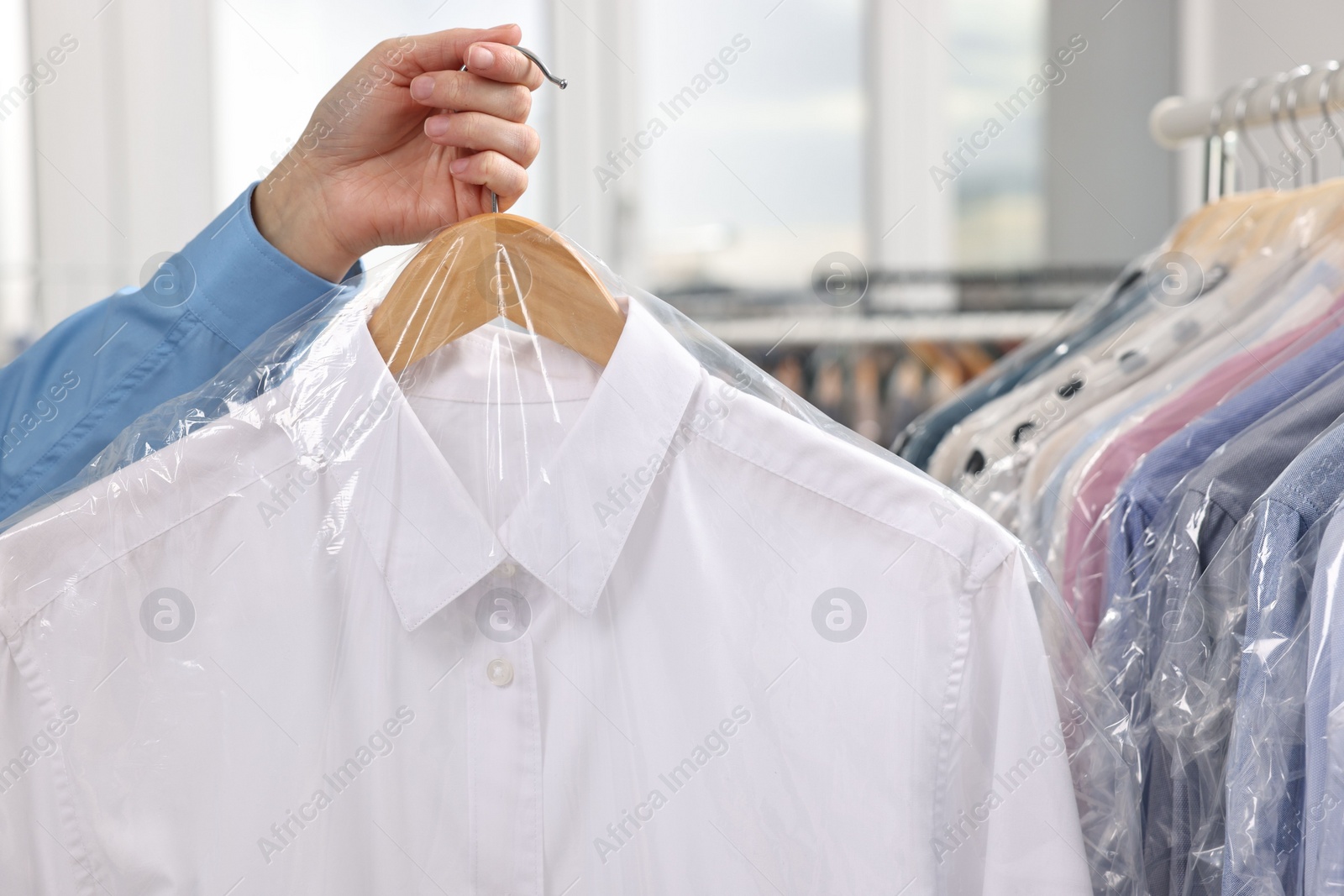 Photo of Dry-cleaning service. Woman holding shirt in plastic bag indoors, closeup