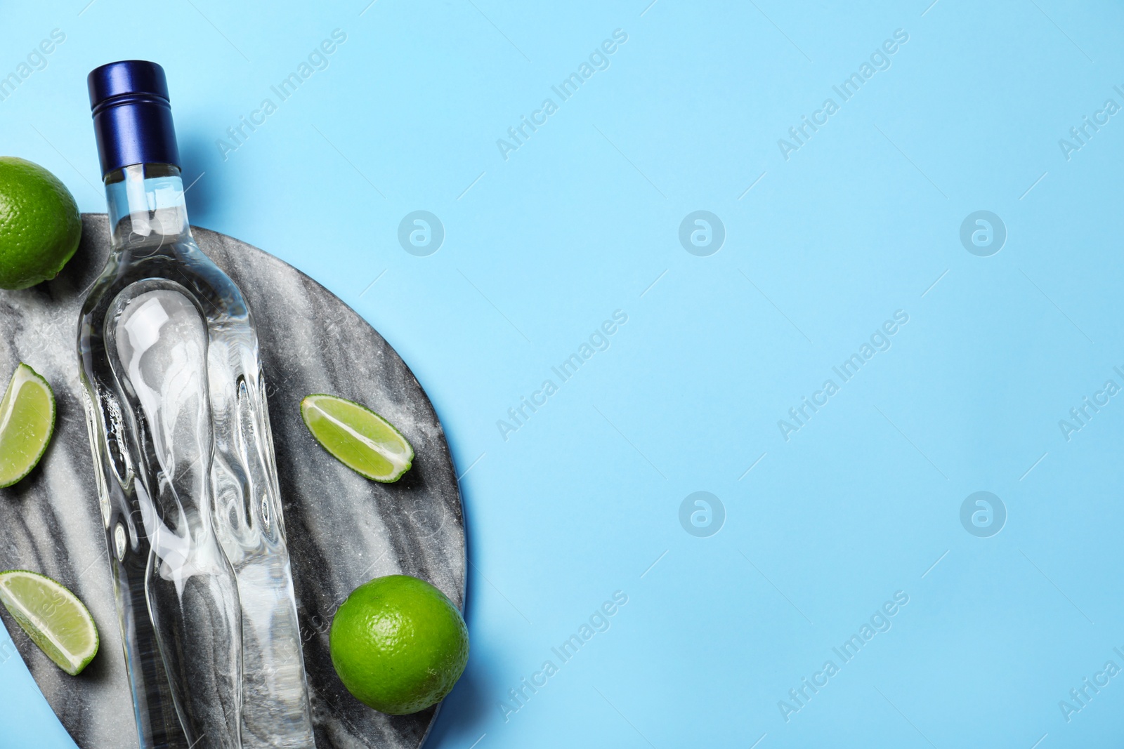 Photo of Bottle of vodka and limes on light blue background, top view. Space for text