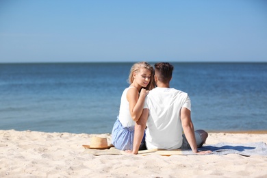 Happy young couple sitting together at beach on sunny day