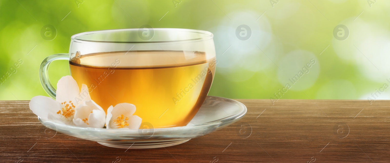 Image of Cup of jasmine tea and fresh flowers on wooden table outdoors, space for text. Banner design