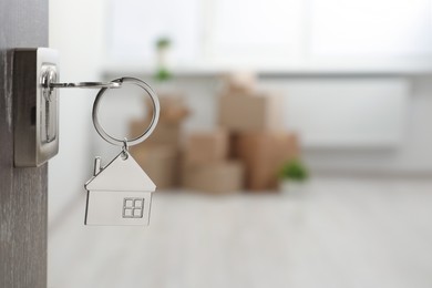 Photo of Mortgage and real estate. Open door with key and house shaped keychain against blurred background, space for text