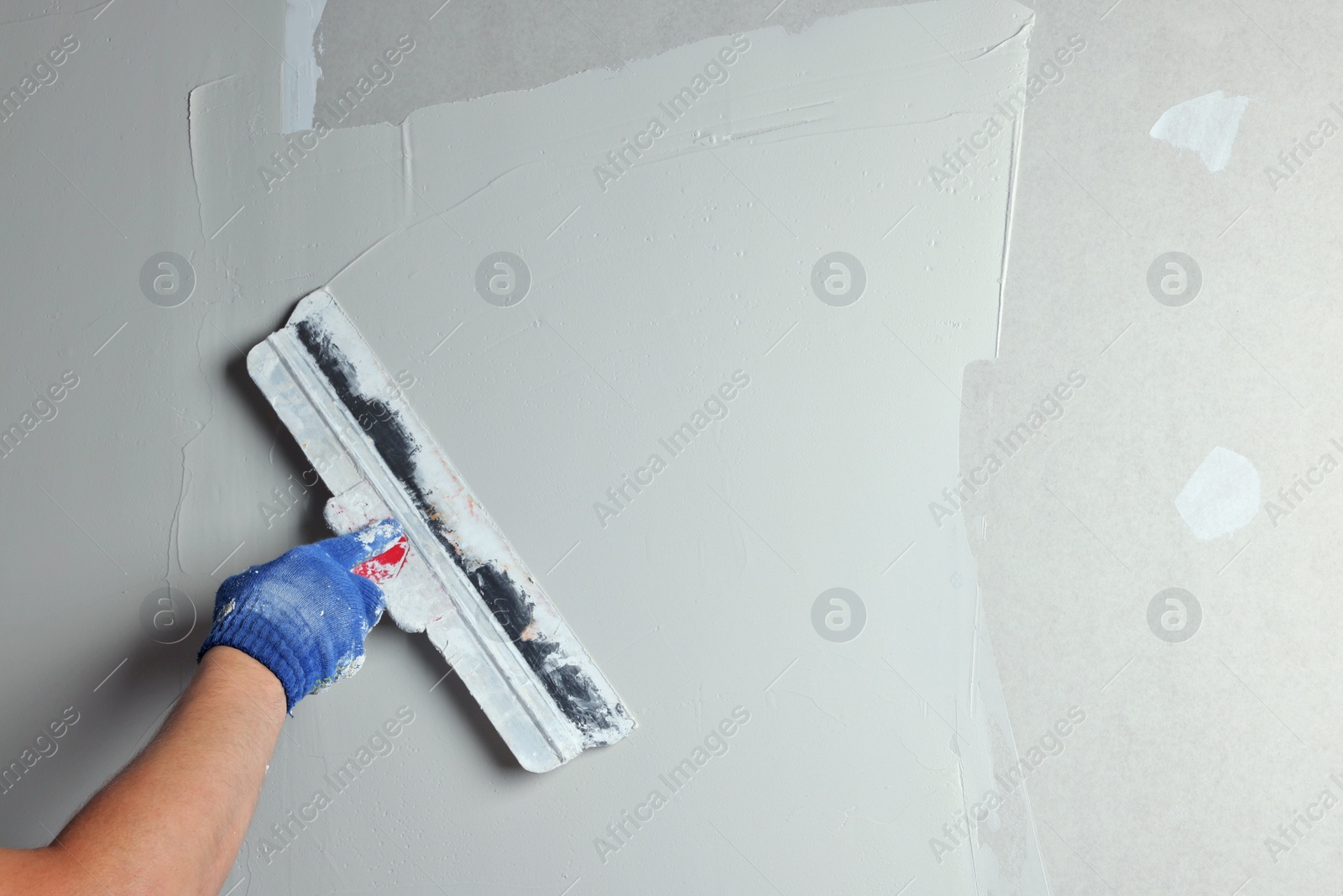 Photo of Professional worker plastering wall with putty knife, closeup