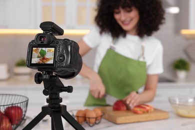 Photo of Food blogger cooking while recording video in kitchen, focus on camera
