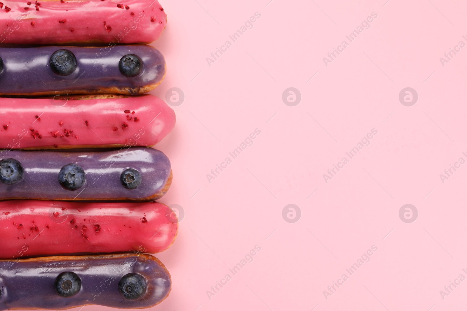 Photo of Delicious eclairs covered with glaze on pink background, top view. Space for text