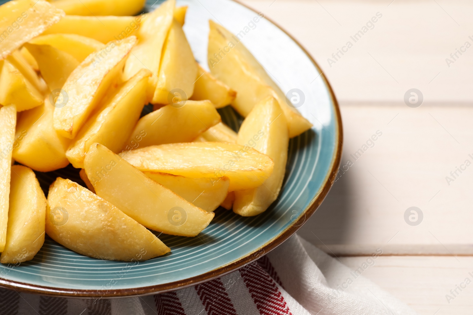 Photo of Plate with tasty baked potato wedges on white wooden table, closeup