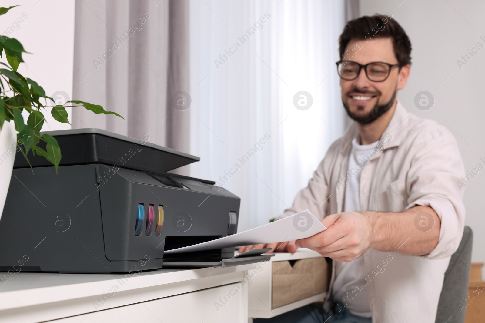 Photo of Man using modern printer at workplace indoors, selective focus