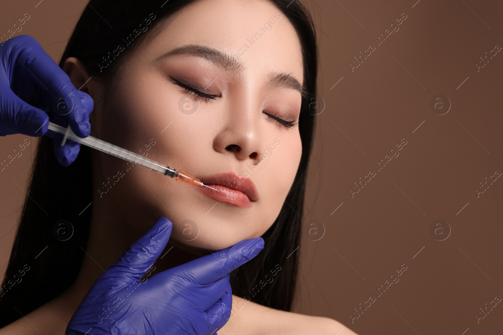 Photo of Woman getting lip injection on brown background, closeup