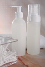 Bottles with face cleansing products and cotton buds on beige marble table