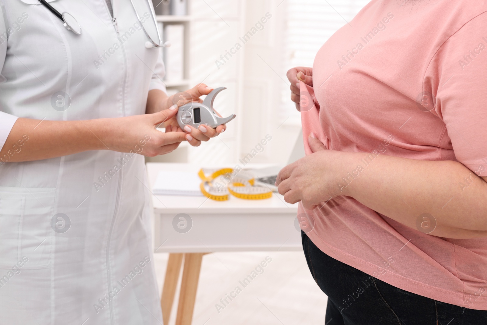 Photo of Overweight woman and nutritionist with digital caliper in clinic, closeup