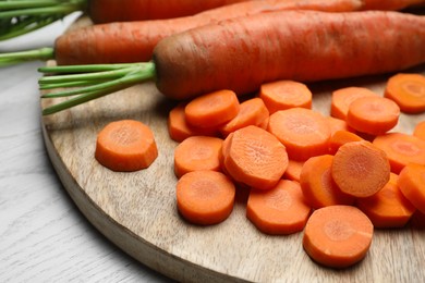 Photo of Whole and sliced fresh ripe juicy carrots on white wooden table, closeup
