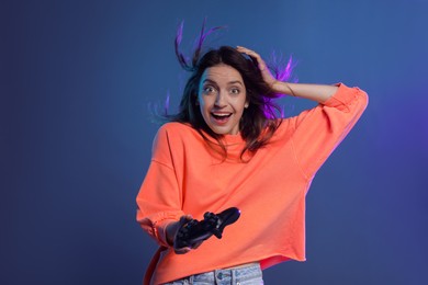 Emotional woman with game controller on dark blue background