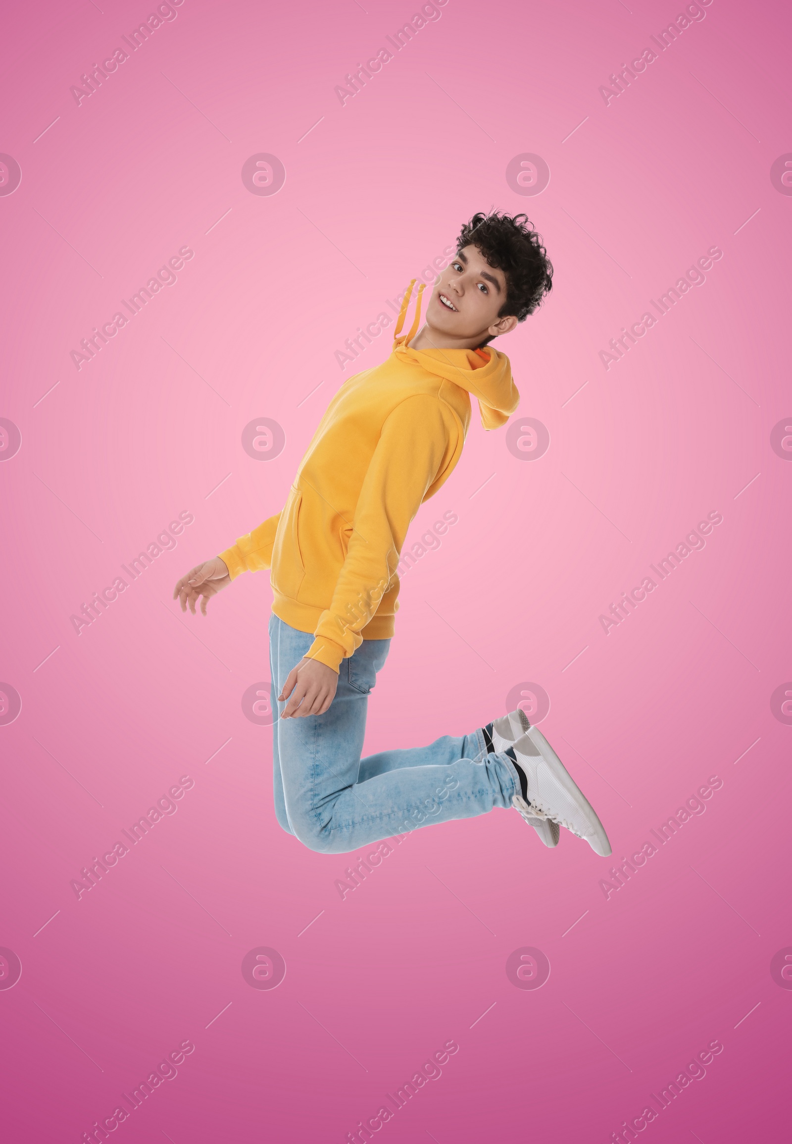 Image of Teenage boy jumping on pink background, full length portrait