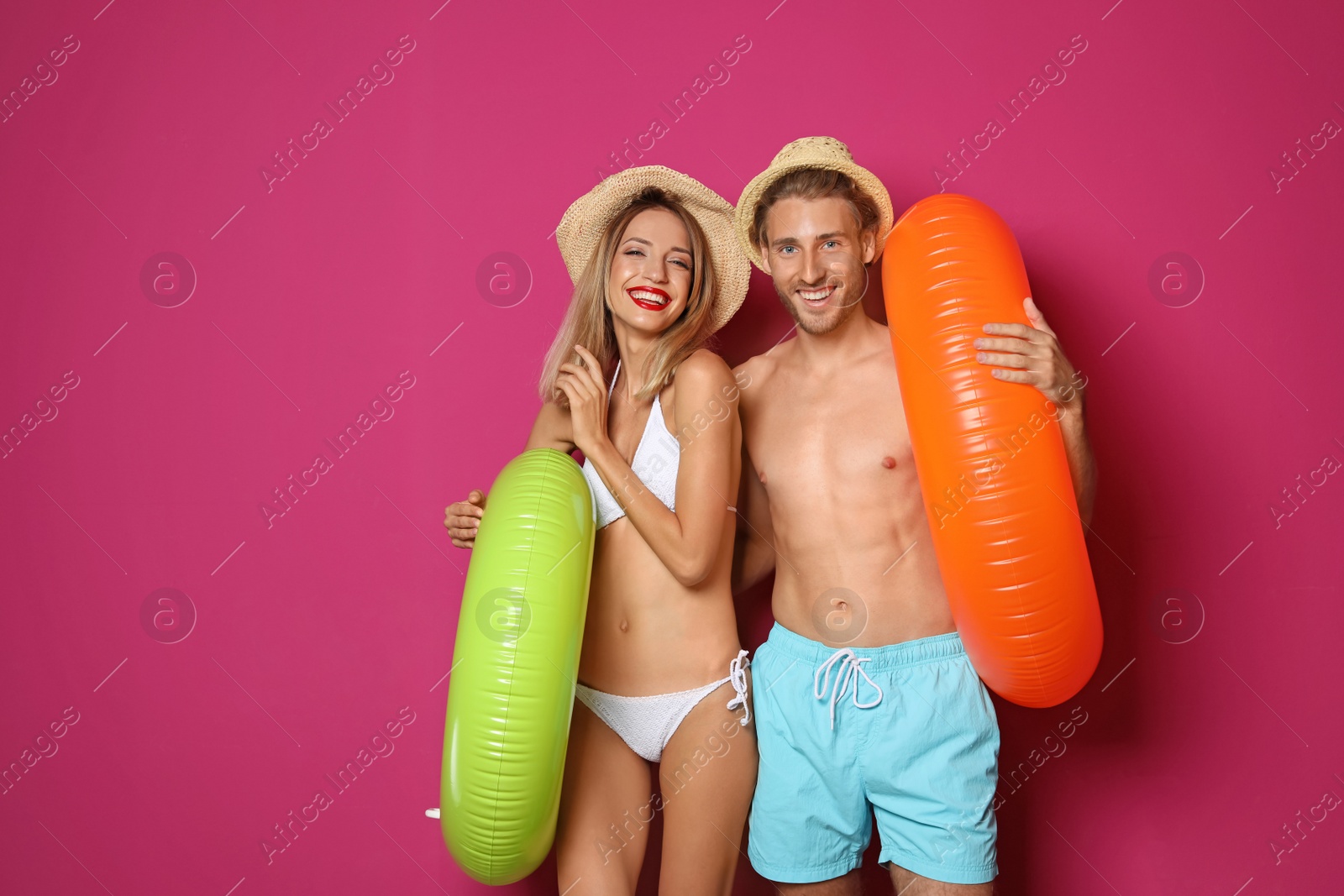 Photo of Happy young couple in beachwear with inflatable rings on color background