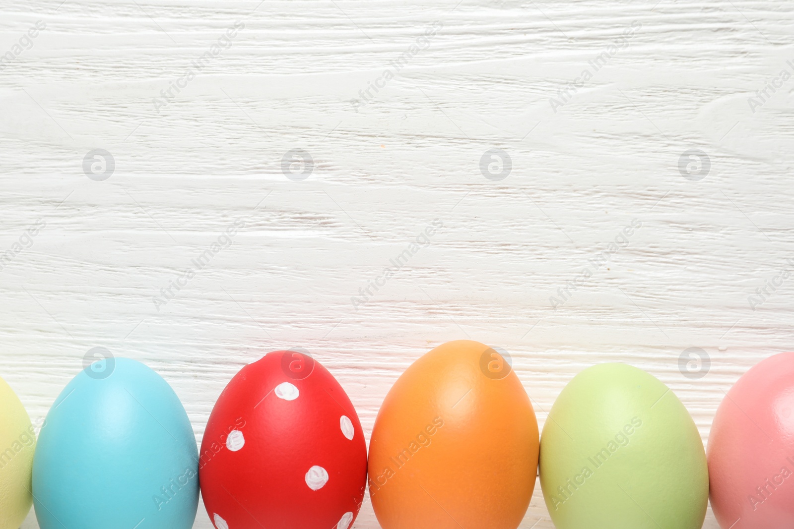 Photo of Flat lay composition of colorful painted Easter eggs on wooden table, space for text