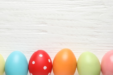 Photo of Flat lay composition of colorful painted Easter eggs on wooden table, space for text