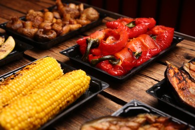 Photo of Plastic containers with different grilled meal on wooden table, closeup. Food delivery service