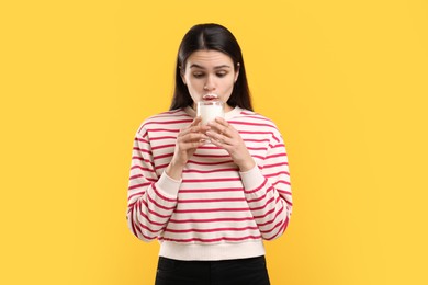 Photo of Cute woman with milk mustache drinking tasty dairy drink on yellow background