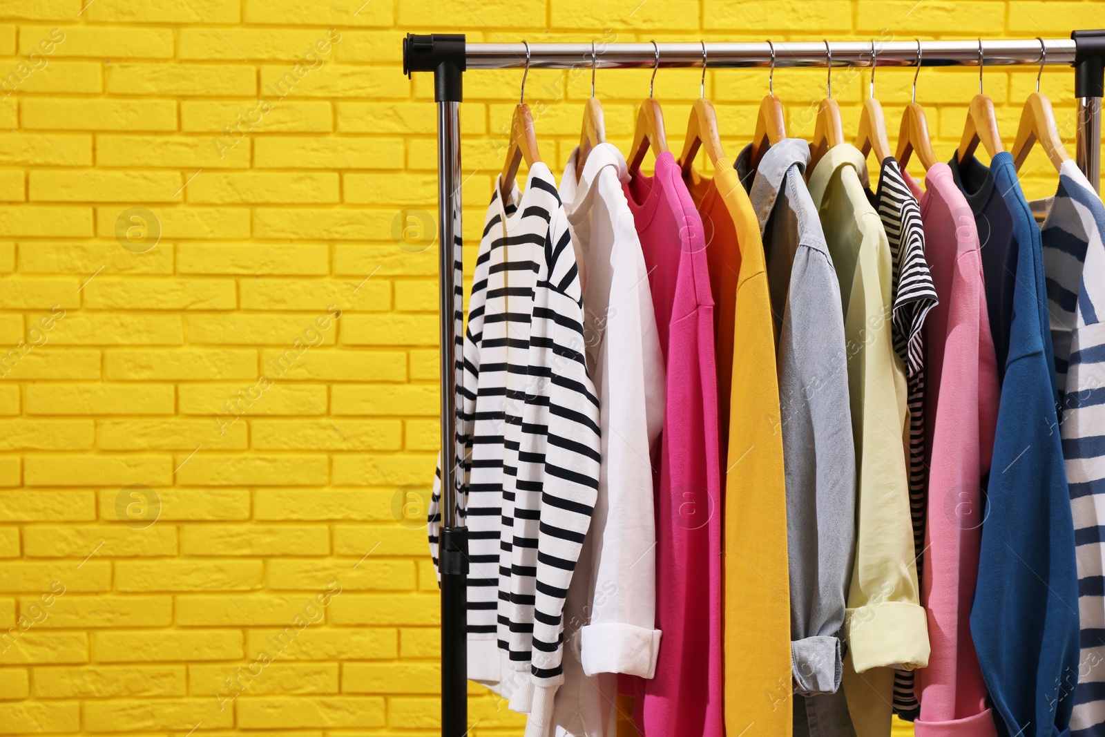 Photo of Rack with different stylish clothes near yellow brick wall. Space for text