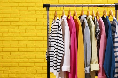 Rack with different stylish clothes near yellow brick wall. Space for text