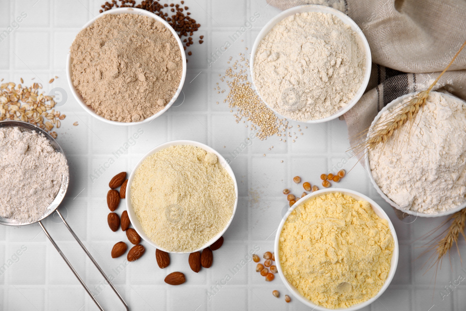 Photo of Bowls with different types of flour and seeds on tiled table, flat lay