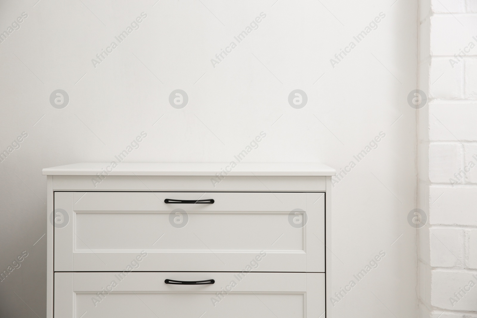 Photo of Modern white chest of drawers near light wall in room, space for text. Interior design