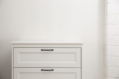 Photo of Modern white chest of drawers near light wall in room, space for text. Interior design